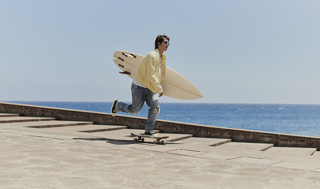 Model skating with a surfboard on his arms in Tenerife for the Harvey Nichols shopping centre summer campaign