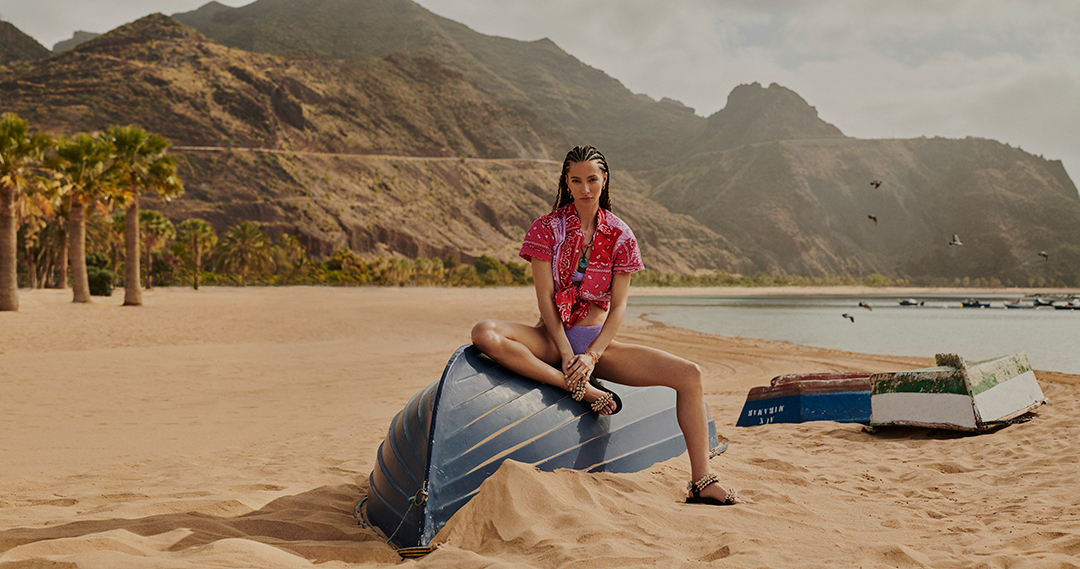 Model sitting on a boat in reverse on a beach in Tenerife for the Harvey Nichols shopping centre summer campaign