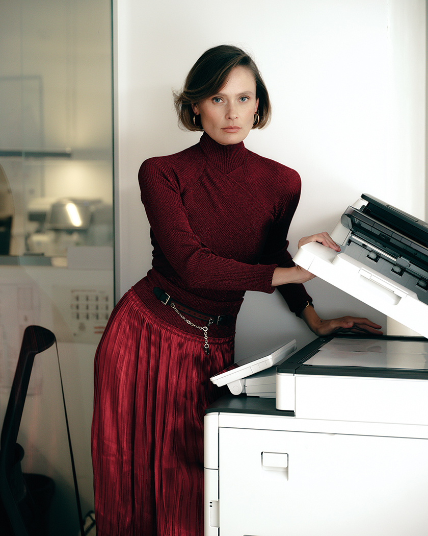 Model dressed in a total red look in an office supported by a printer for Instyle Spain 