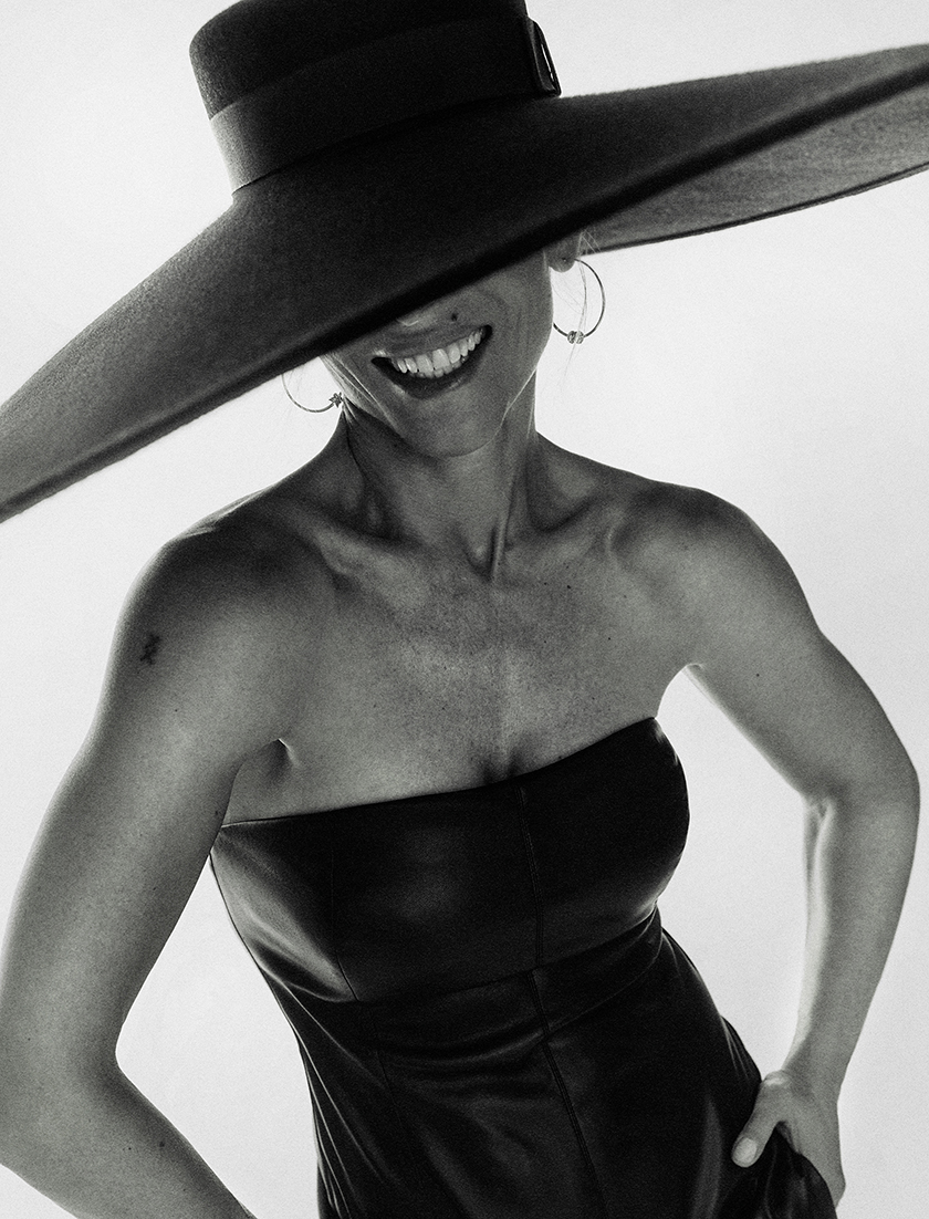 Black and white image of Elsa Pataky smiling for the editorial of Instyle Spain styled by Francesca Rinciari wearing a strapless leather jumpsuit from Philosophy di Lorenzo Serafini and a wide-brimmed hat from Nina Ricci. 