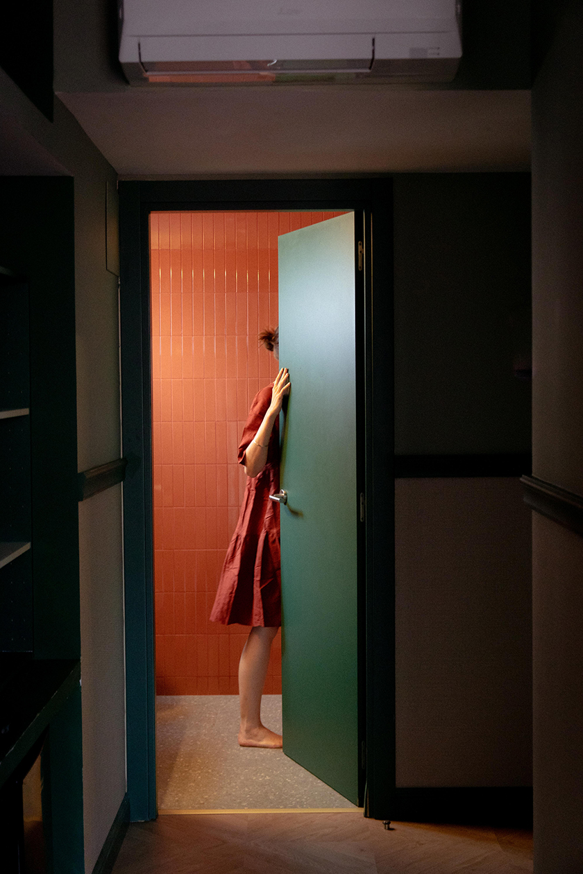 Photograph of a girl in a red dress inside the bathroom of one of the hotel rooms. 