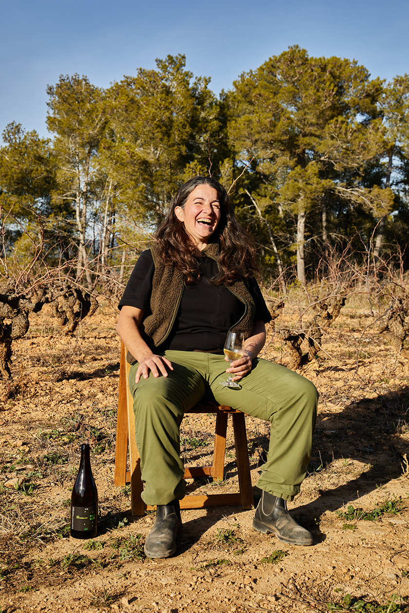 A woman seated on a chair laughing with a bottle of wine