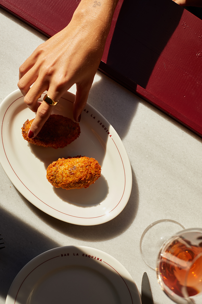 A hand picking up a croquette from a plate in La Esquina bar.