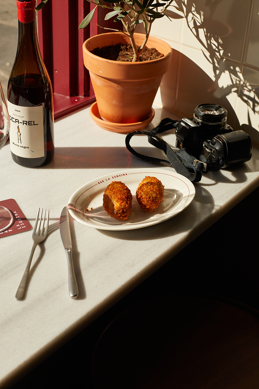 Bar at La Esquina bar with a plate of croquettes, a glass of wine and a camera. 