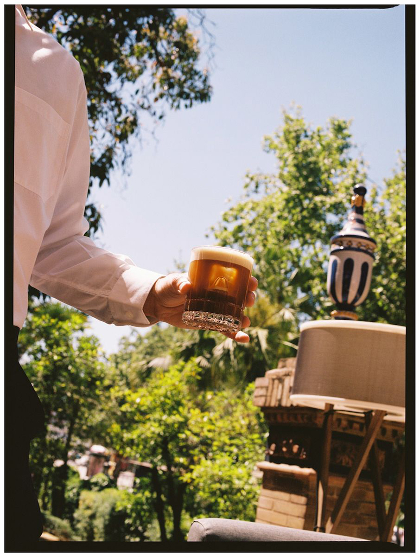 Waiter carrying a glass with a cocktail in the garden.