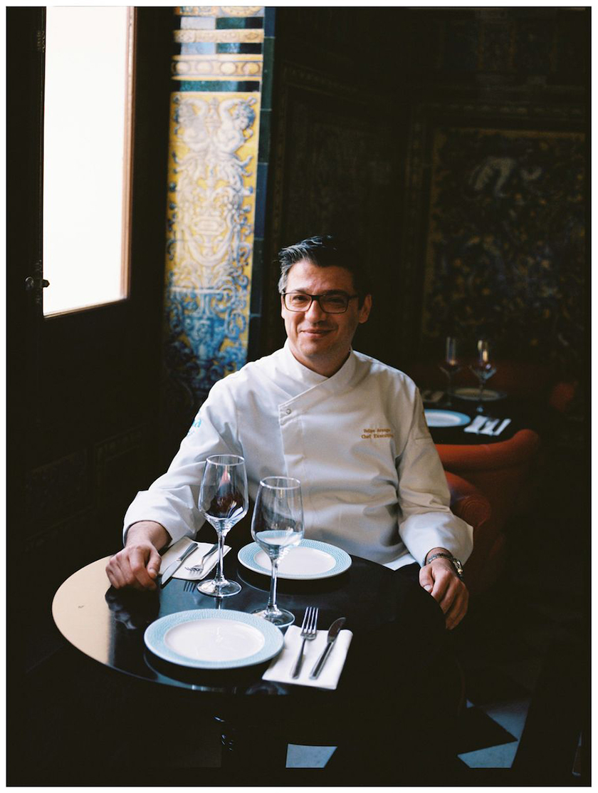 Smiling man sitting at a table set with plates and glasses from the Hotel Alfonso XIII. 