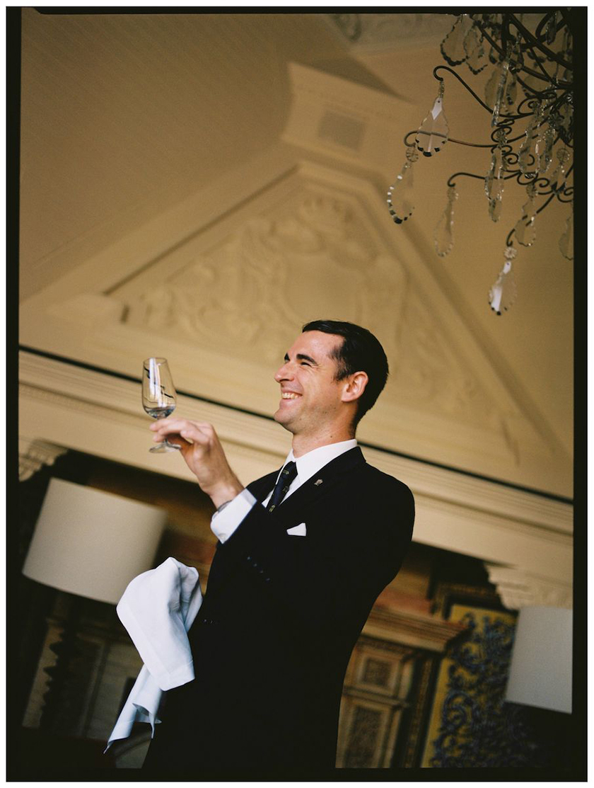 Worker of the Hotel Alfonso XIII in suit holding a glass and smiling 