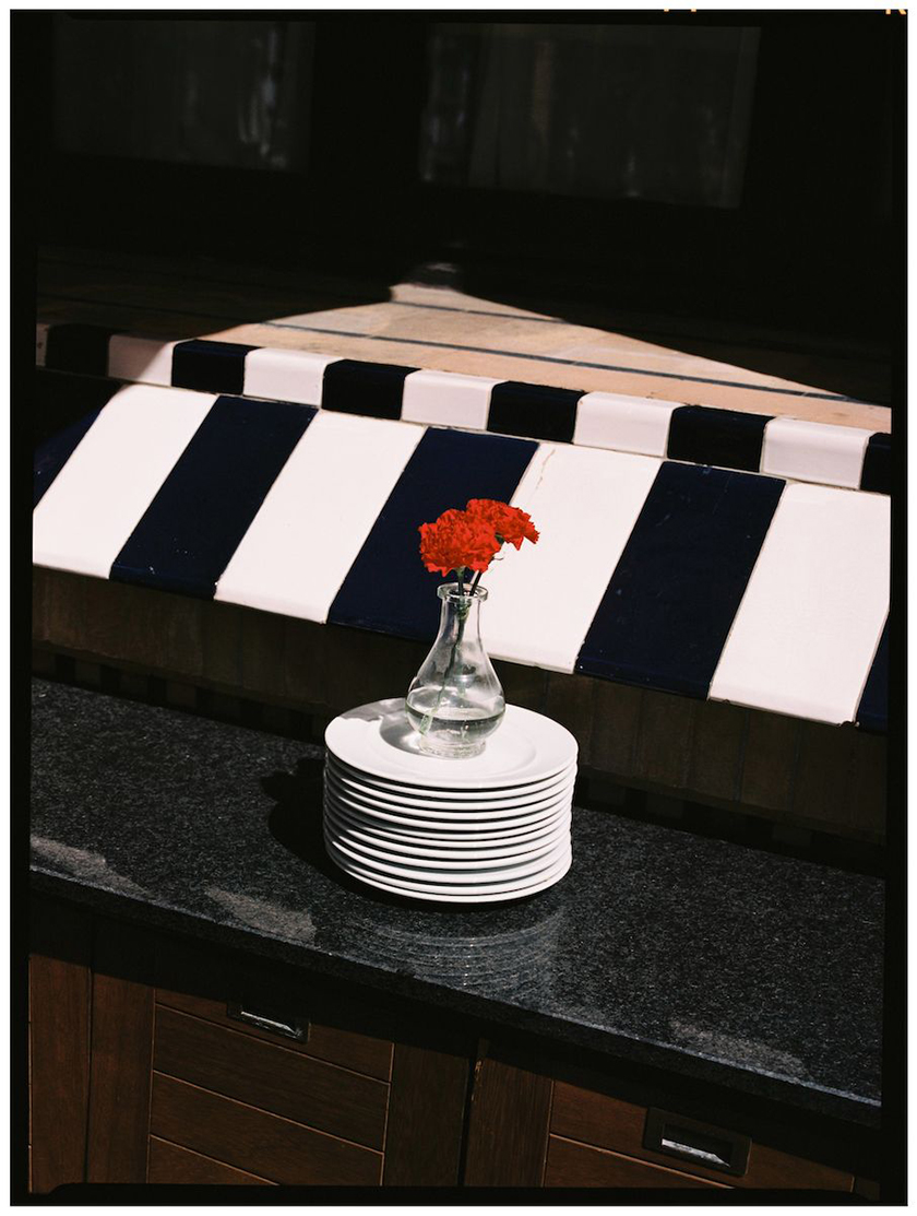 Pile of plates with a vase and a red flower on top of it.