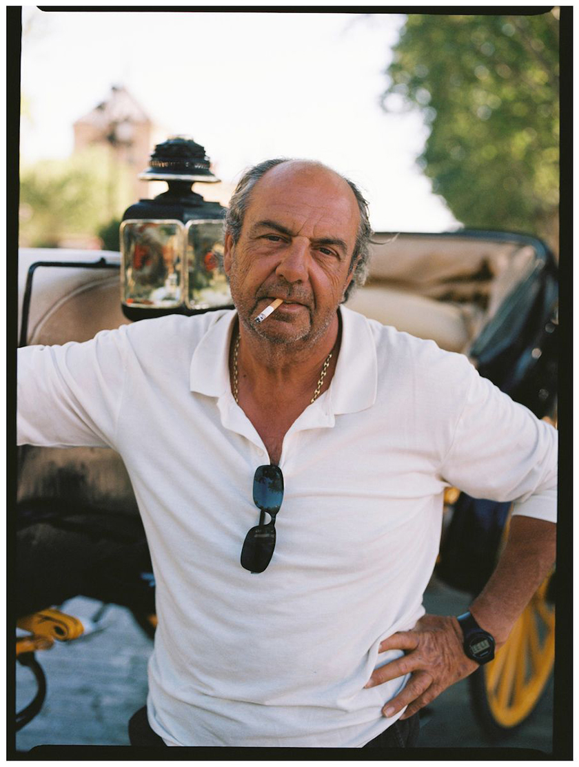 Man with a white t-shirt and a cigarette in his mouth looking at the camera.