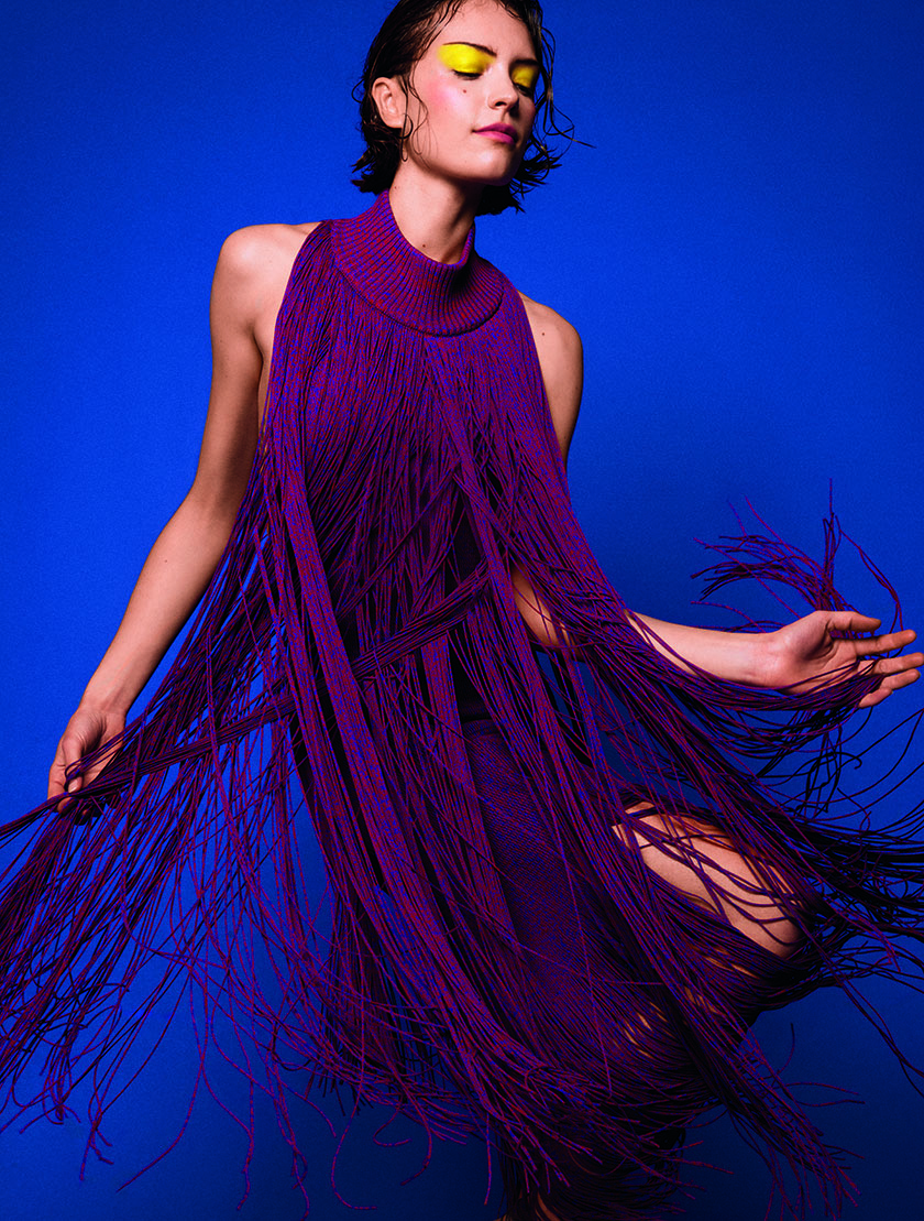 Model on a blue background dancing with dressed in a lilac burrberry honoring fashion in motion. 
