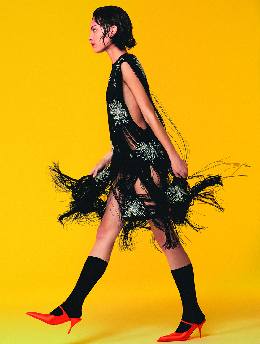 Image of the model walking in a fringed dress on a yellow background homneage to fashion in motion. 