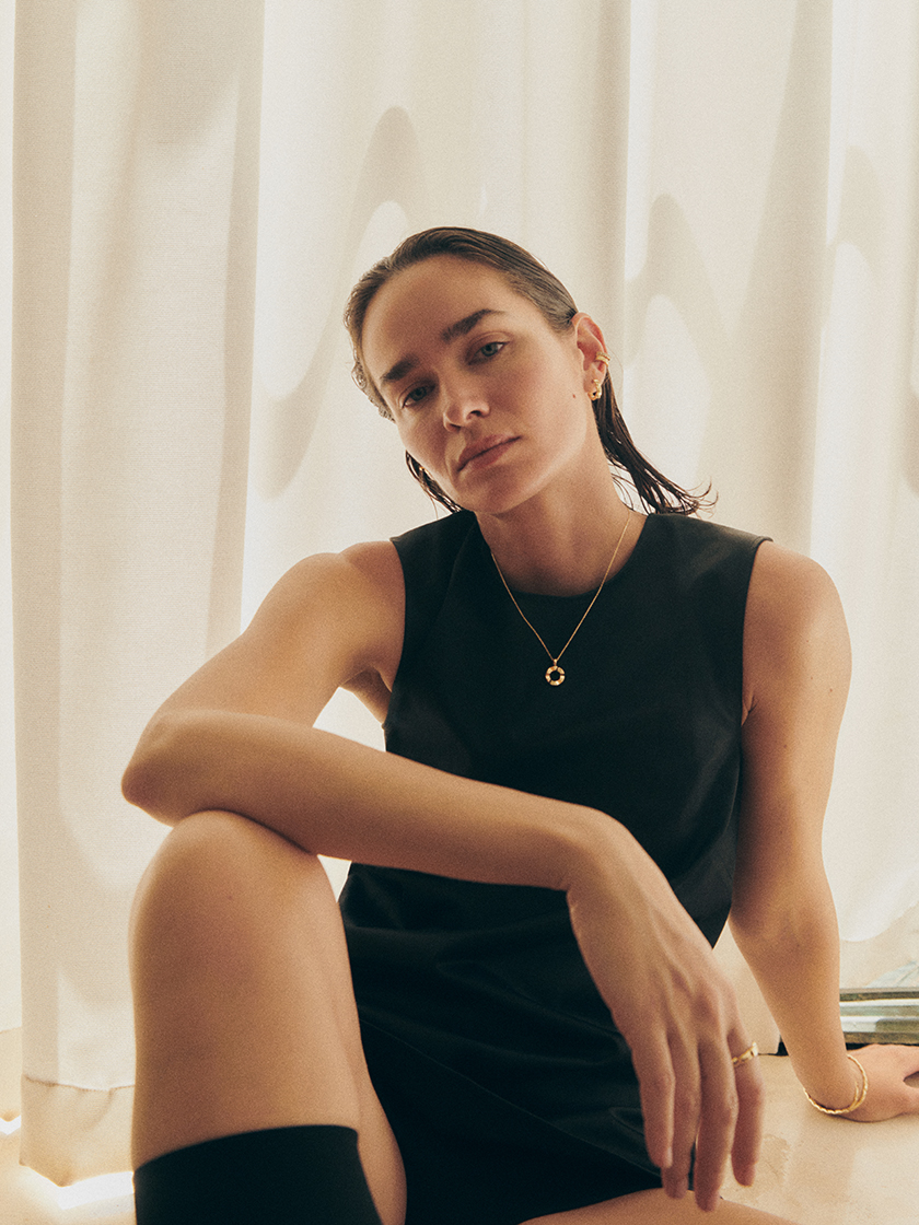 Image of the model sitting on the floor with her legs bent wearing a necklace from the new Prunés campaign. 