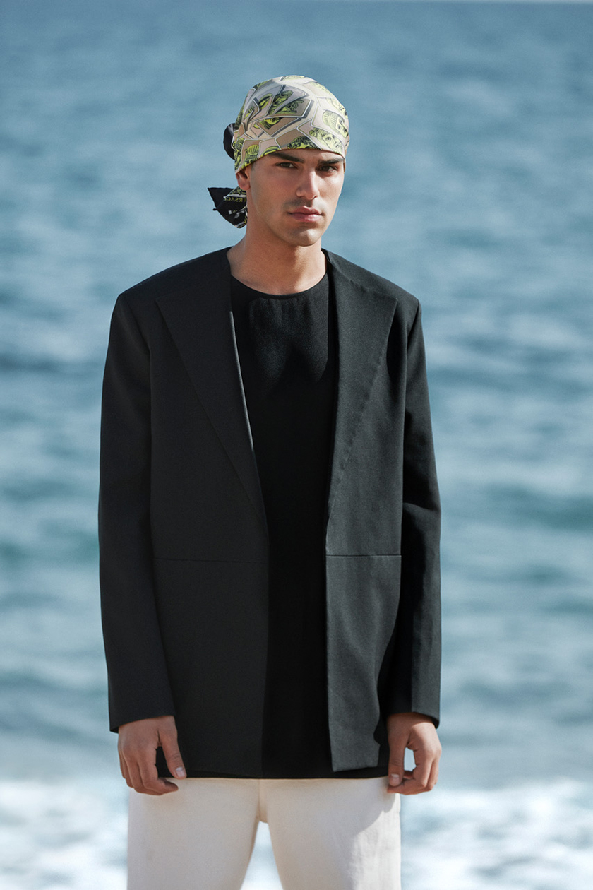 A boy in front of the sea, wearing a headscarf and a black jacket