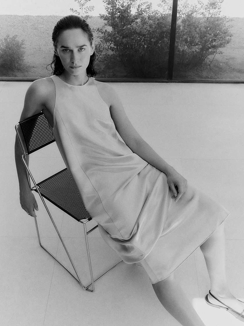 Black and white image of the model sitting in a chair wearing a necklace from the new Prunés campaign. 