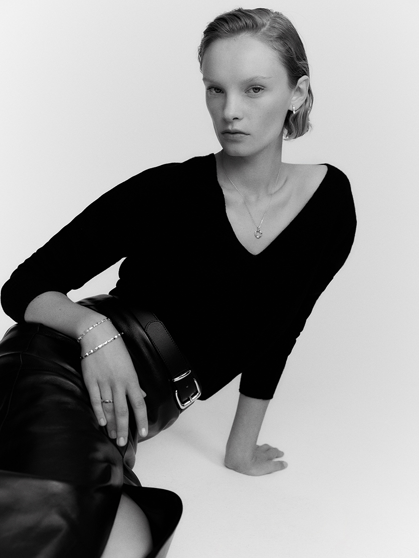Black and white photo, a woman on the ground in an elegant pose showing the jewellery she is wearing. 