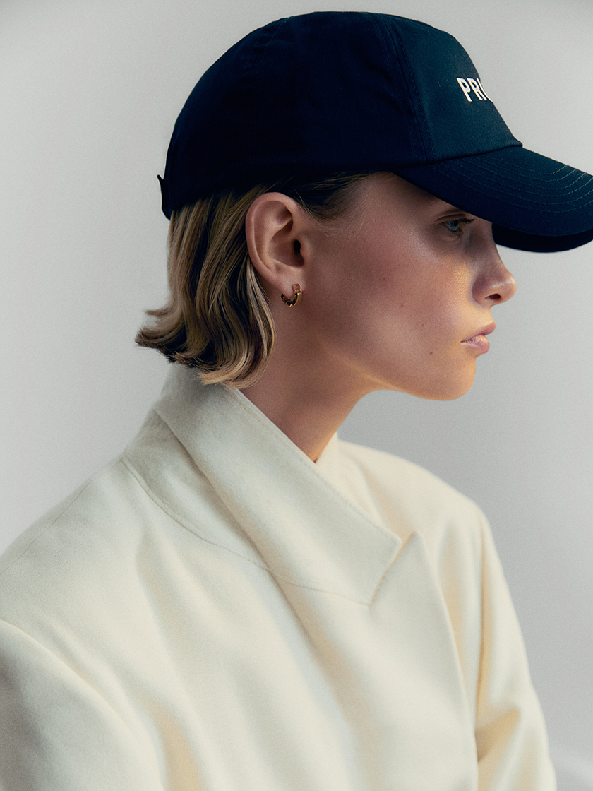 Woman in profile, wearing a cap and branded earrings. 