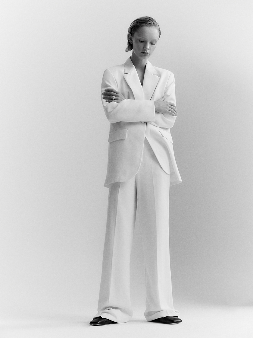 Full-length black and white photo of a woman in a white suit looking at the ground. 