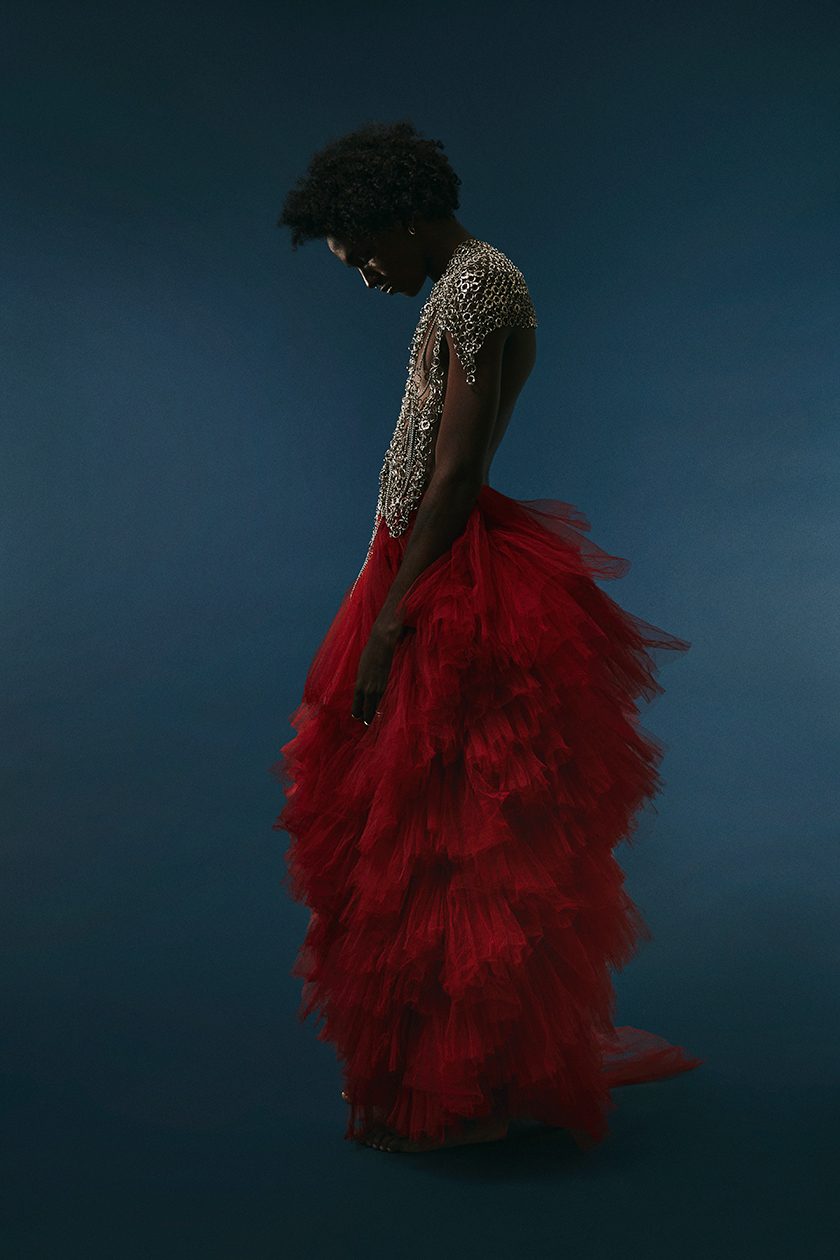 A man in a red tulle dress, looking at the floor for Herdes Magazine. 