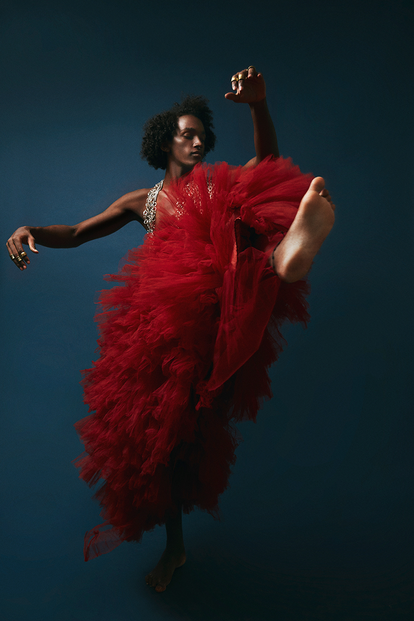 Full shot of a boy dancing in a very extravagant red dress for Herdes magazine. 