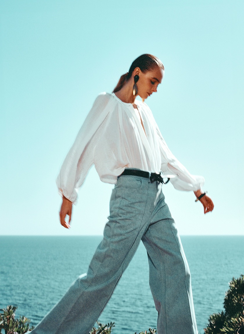 Model walking among bushes with the sea in the background wearing a shirt and pants from the new campaign of The label edition.