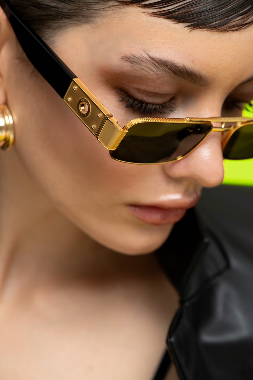 Close-up of Linda Farrow's glasses worn by a model on a green background. 