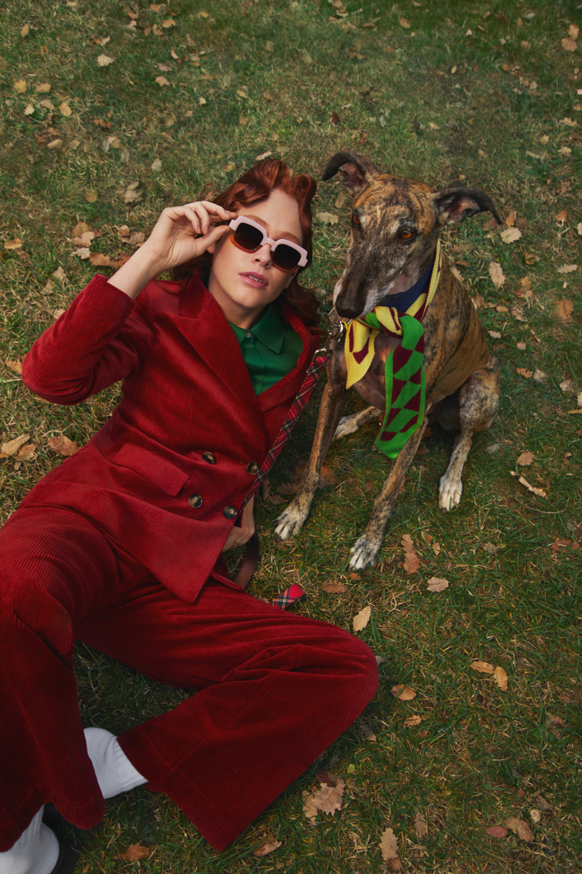 Model standing next to a dog wearing a red velvet suit and glasses from the new collection of the brand Woodys. 