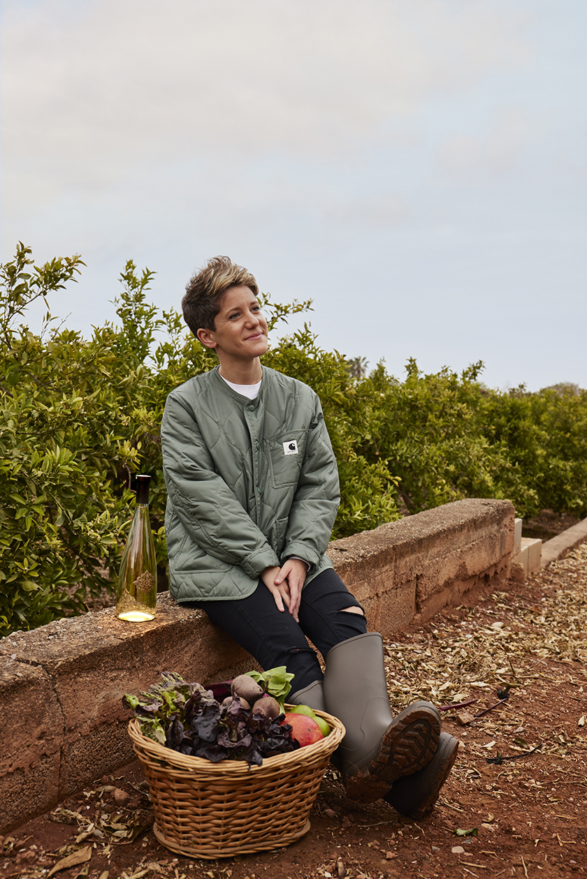 The chef Vicky Sevilla sitting on the wall of her vegetable garden with freshly picked vegetables. 