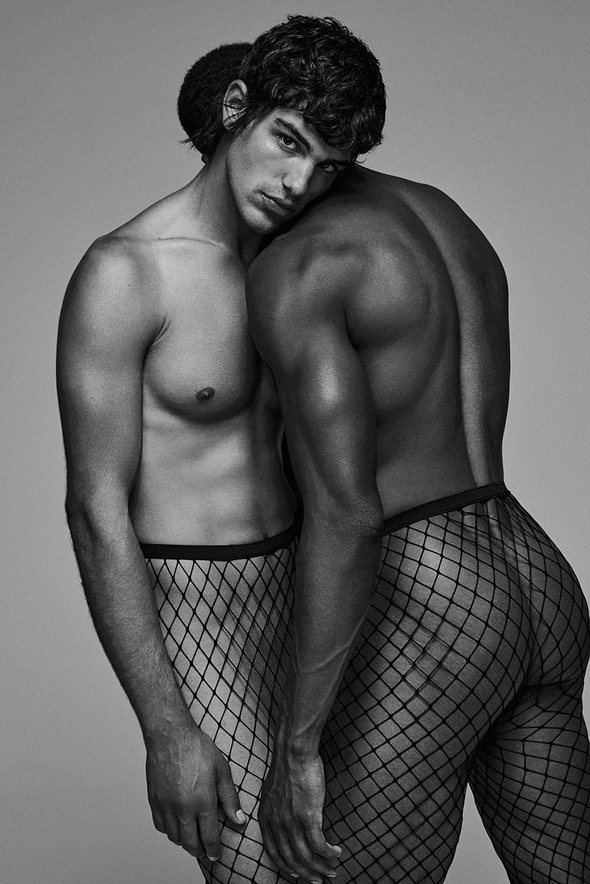 A couple of two boys dressed in fishnet stockings leaning on top of each other.