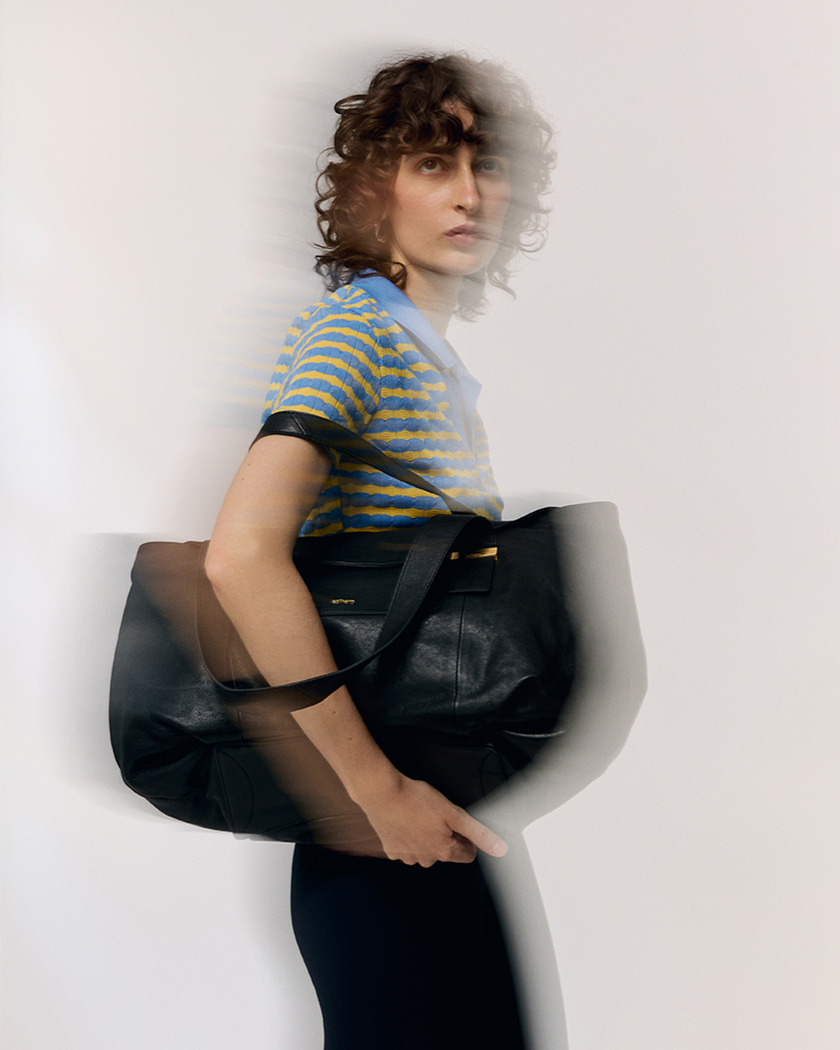 Blurred image with a model holding a black bag from the launch campaign.