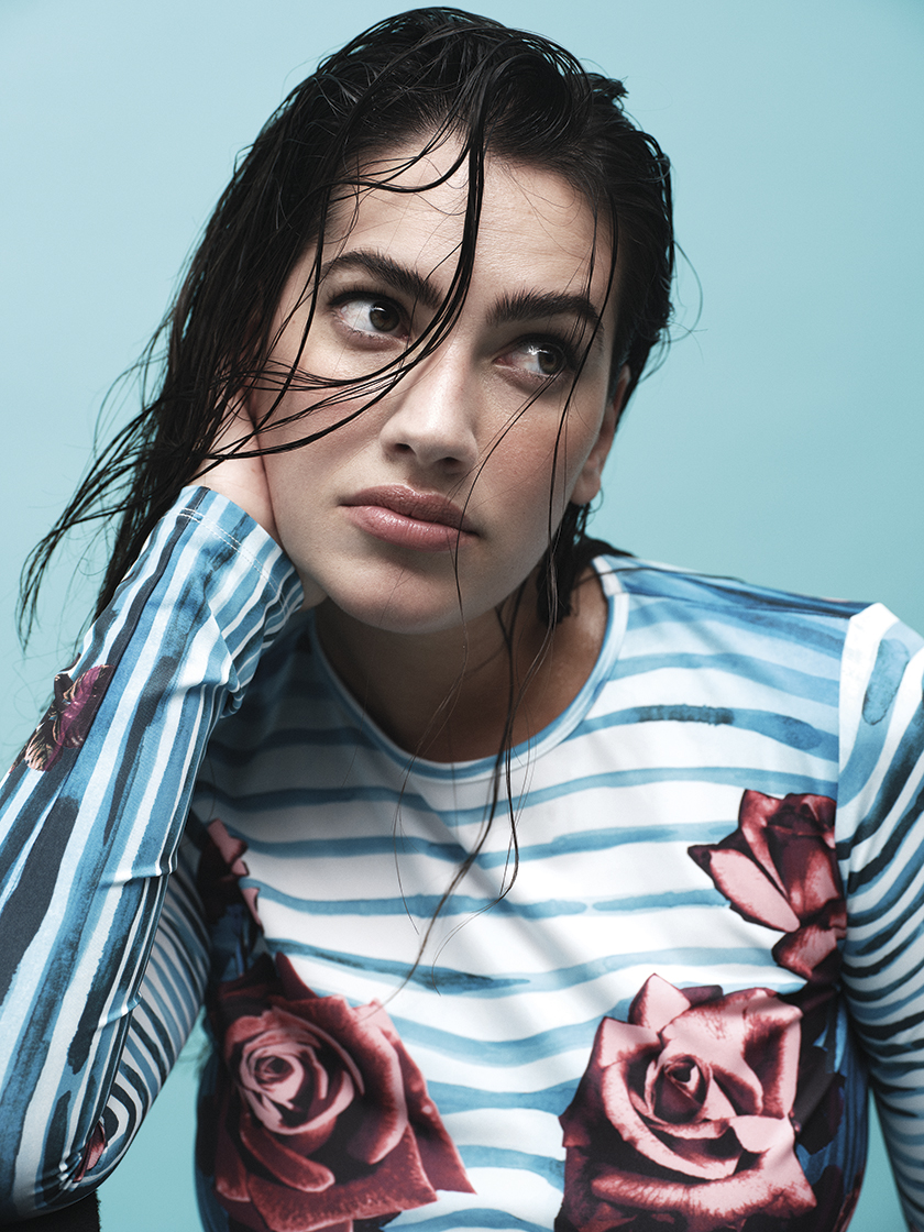 short shot of Lorena Duran looking out of the corner of her eye in a blue dress and blue background. 