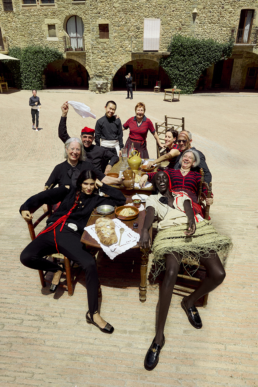 Group of Sardinian dancers seated at a table in the plaza of a typical Catalan village with two models in the front row. 