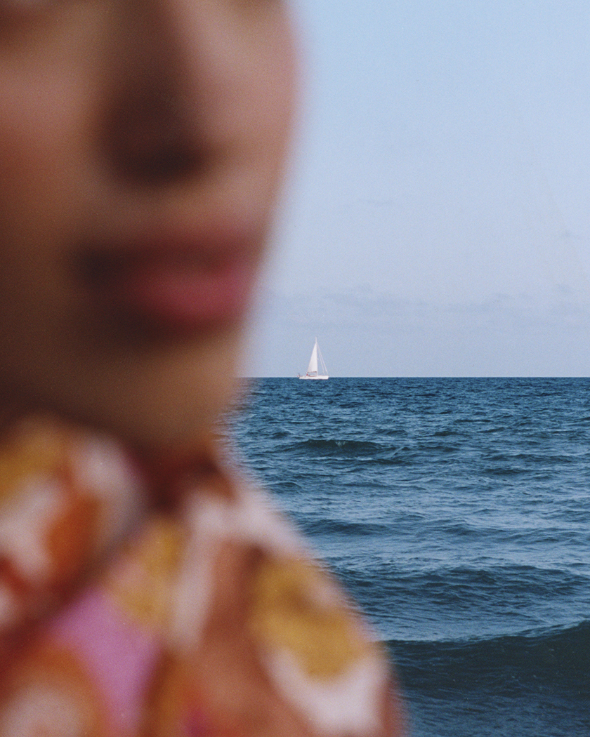 Model's face out of focus in the foreground with the focus on the sea and a boat in the background