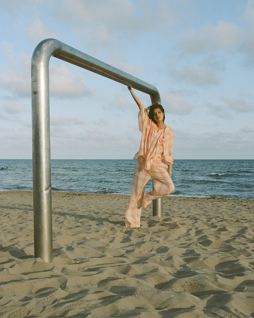 Model wearing a dress from the launch of The label edition's summer collection leaning on a metal pole.  