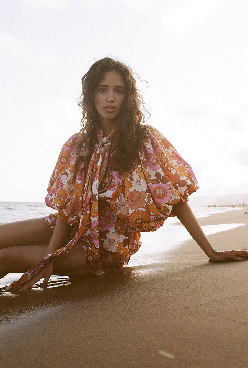 Model sitting on the seashore at sunset wearing a dress from the latest launch of the brand The label edition. 