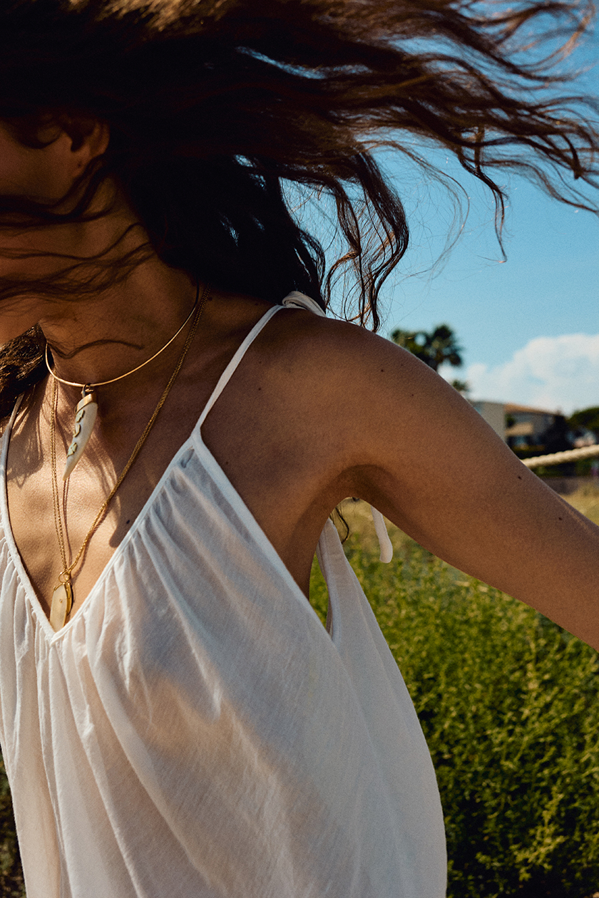 Close-up profile shot of the model's face running through the countryside in a white dress. 