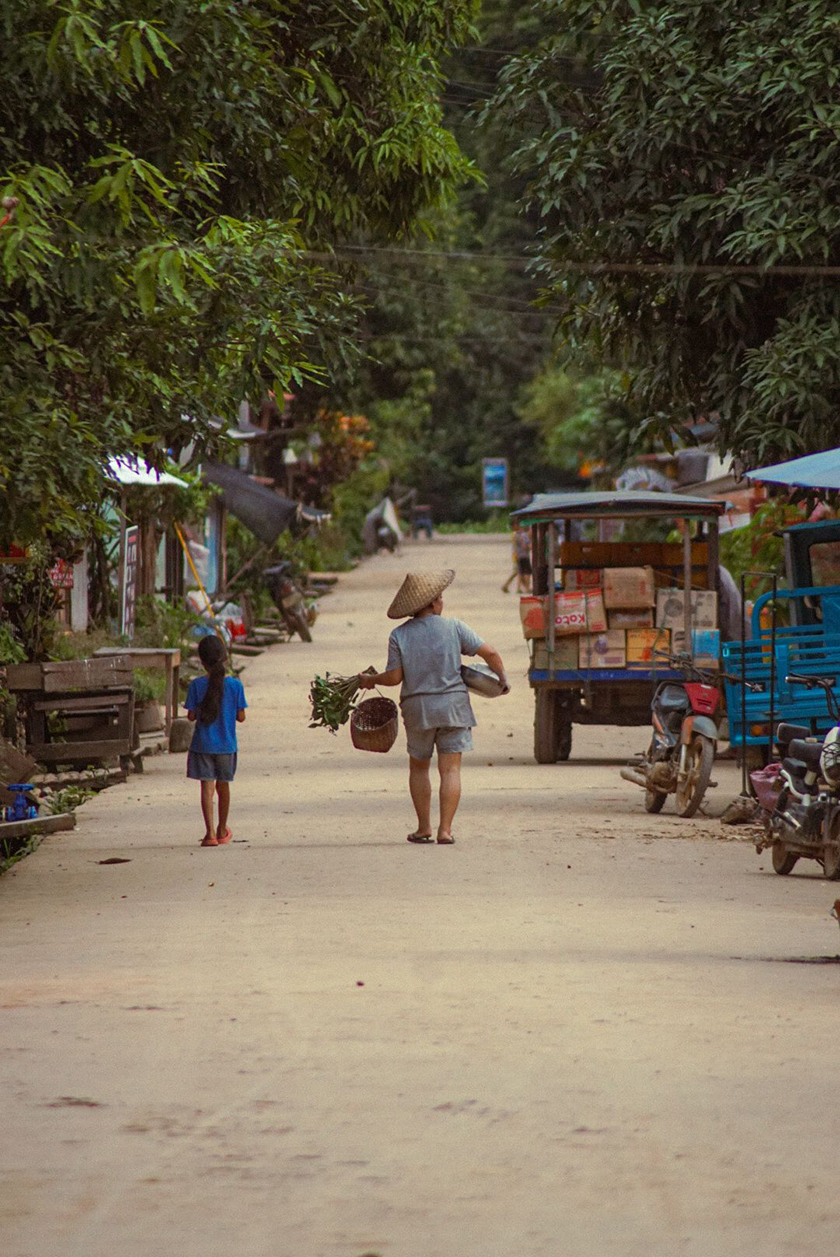 People walking along a street in a village in Vietnam with different types of vegetables. 