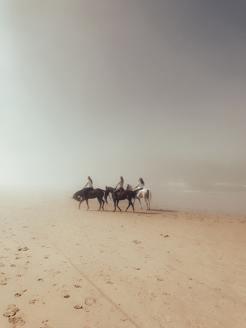 People riding horses on a foggy beach.