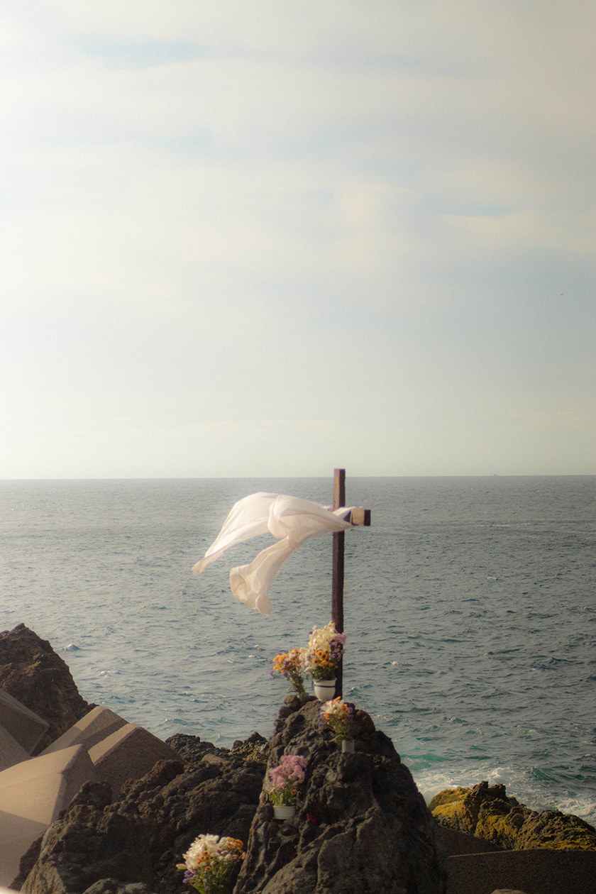 Cross and flowers on a tombstone with a white veil overlooking the sea 