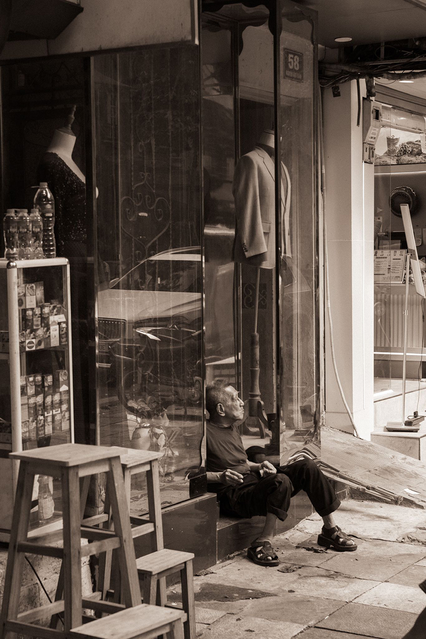 Black and white photo of a person sitting in a shop window.