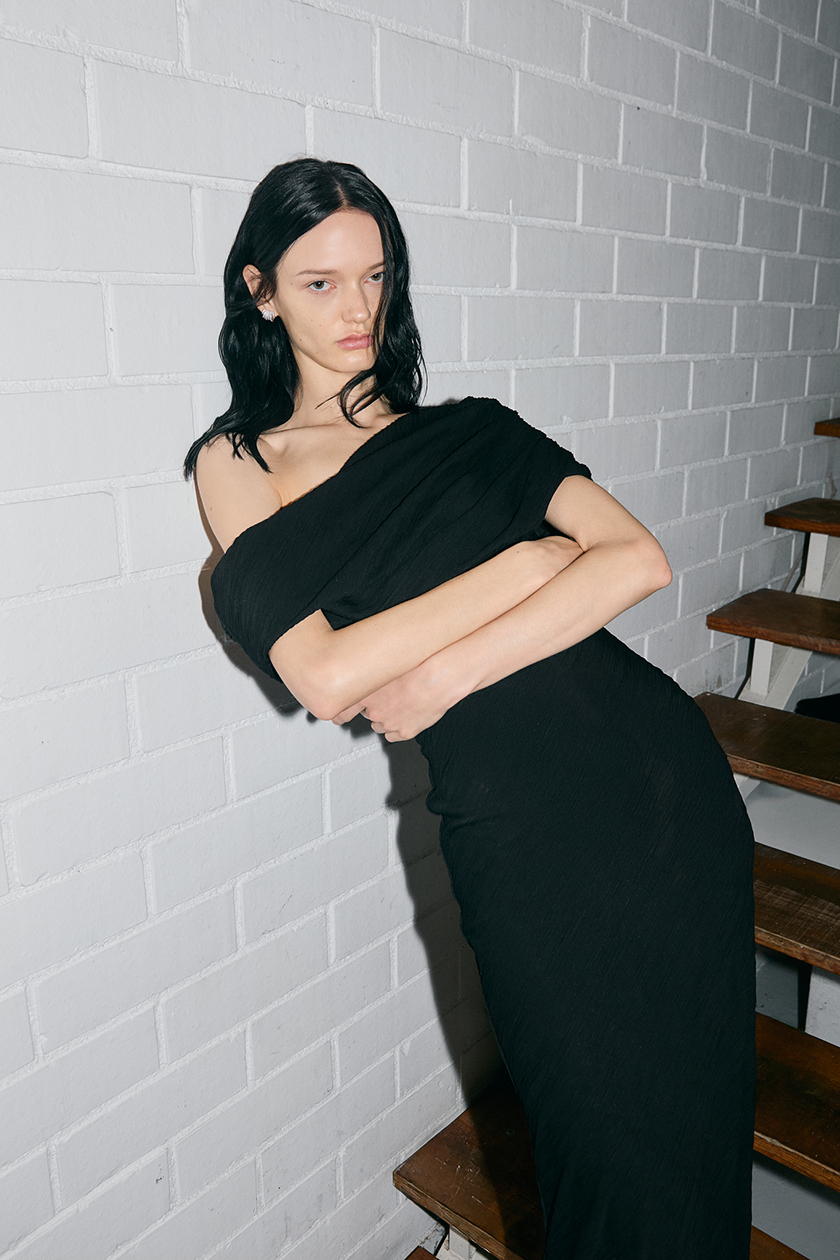 Model leaning against a white wall wearing a black ZeGarcia dress.