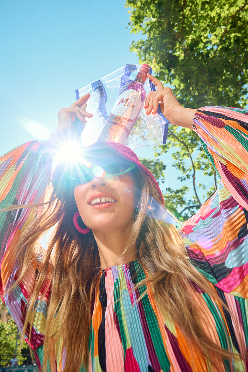 Counter-cropped photo with sunlight across the face of the model holding a bottle of wine in a bag.