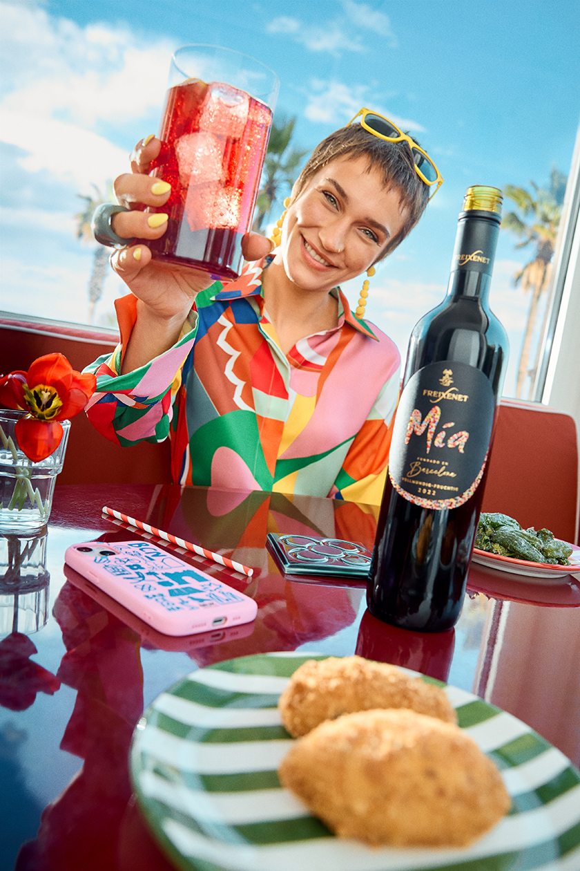 Image of a table full of food with a bottle of Freixenet's Mía brand wine, with a model sitting at a table having a tinto de verano.