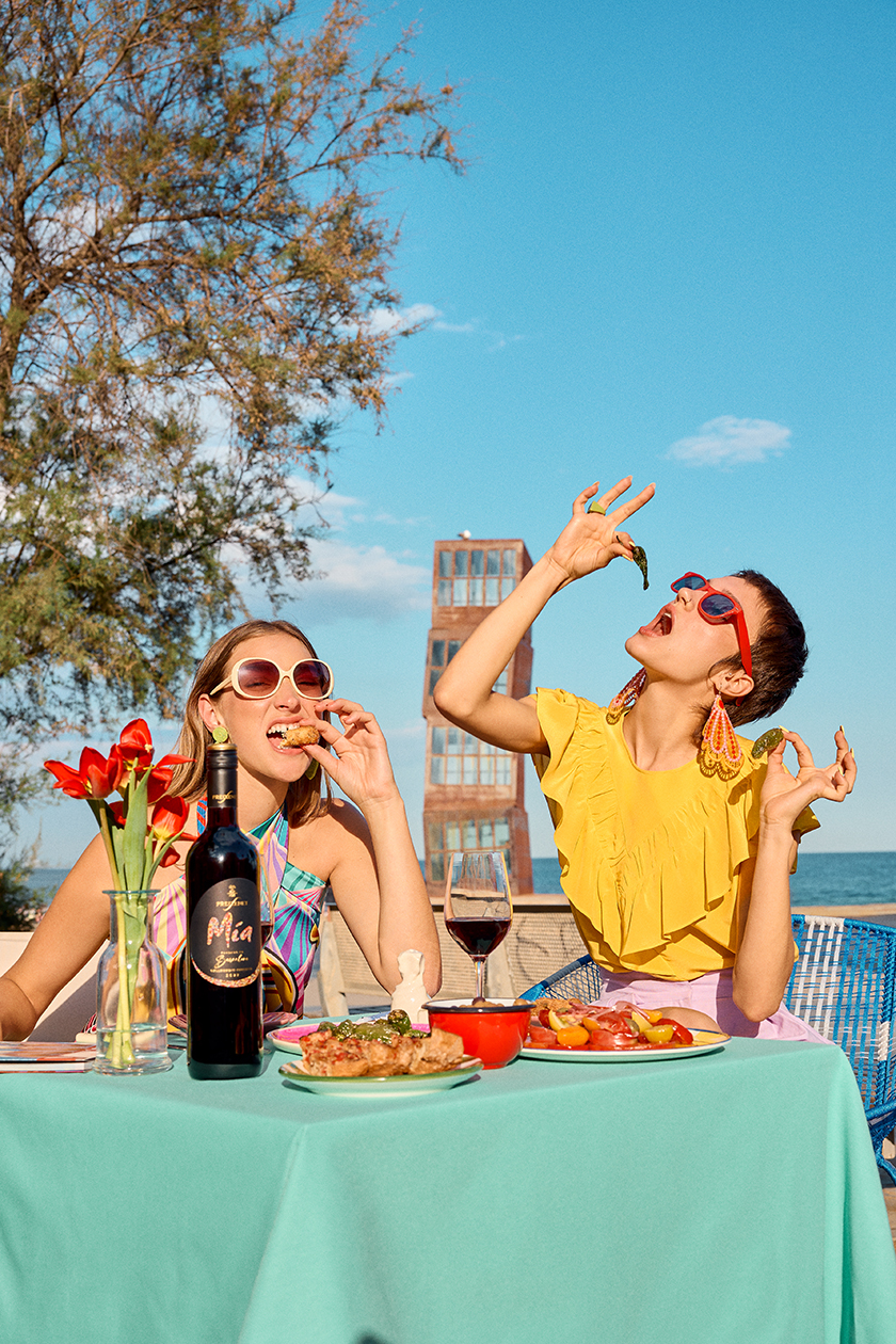 Image of a table full of food with a bottle of Freixenet's Mía brand wine, with two models sitting at a table doing funny poses while eating.